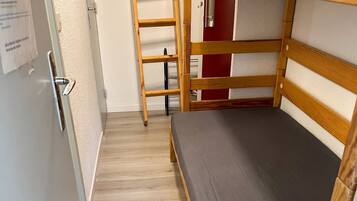 A bunk bed with a wooden ladder, a grey mattress, and a wooden floor.