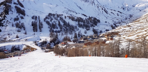 A snow-covered mountain village with buildings, a ski lift, and a winding road. - Homerez - Studio Allos - Mountain view (Allos)