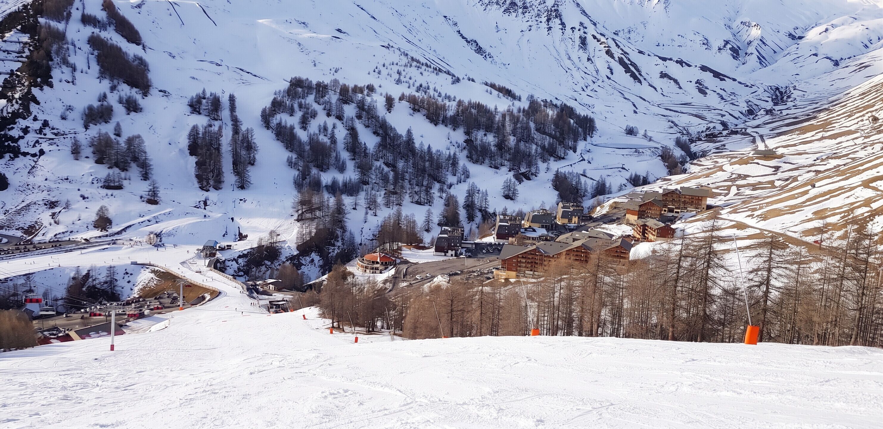 Une ville de montagne enneigée, avec des bâtiments, une piste de ski et une zone boisée.