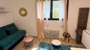 A living room with a teal sofa, a small round table, a blue rug, a ceiling light fixture, and a window with curtains. - Homerez - Studio Allos - Mountain view (Allos)
