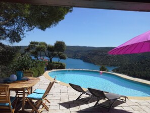 Ein Poolbereich mit Liegestühlen und einem Tisch mit Blick auf einen See und Hügel.