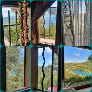 Panoramic views of a serene lake and rolling hills from a spacious room with a large window.