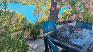 A table and chairs set outdoors with a view of a lake and hills in the background. - Architect's house, rustic style, will seduce you by its environment  (Esparron-De-Verdon)