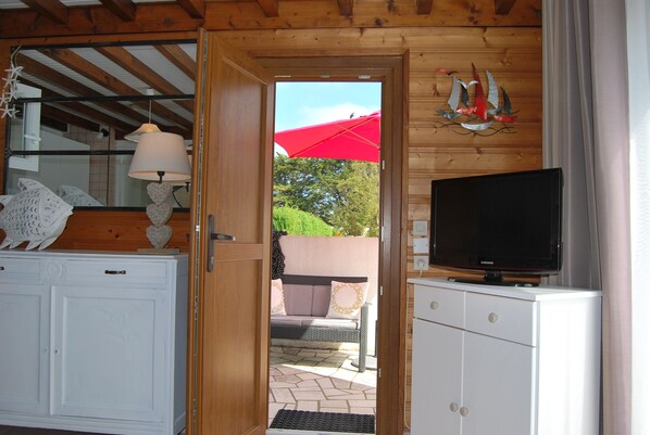 A wooden interior with a television on a cabinet, a door leading to an outdoor area with a red umbrella, and a wall-mounted decorative piece.