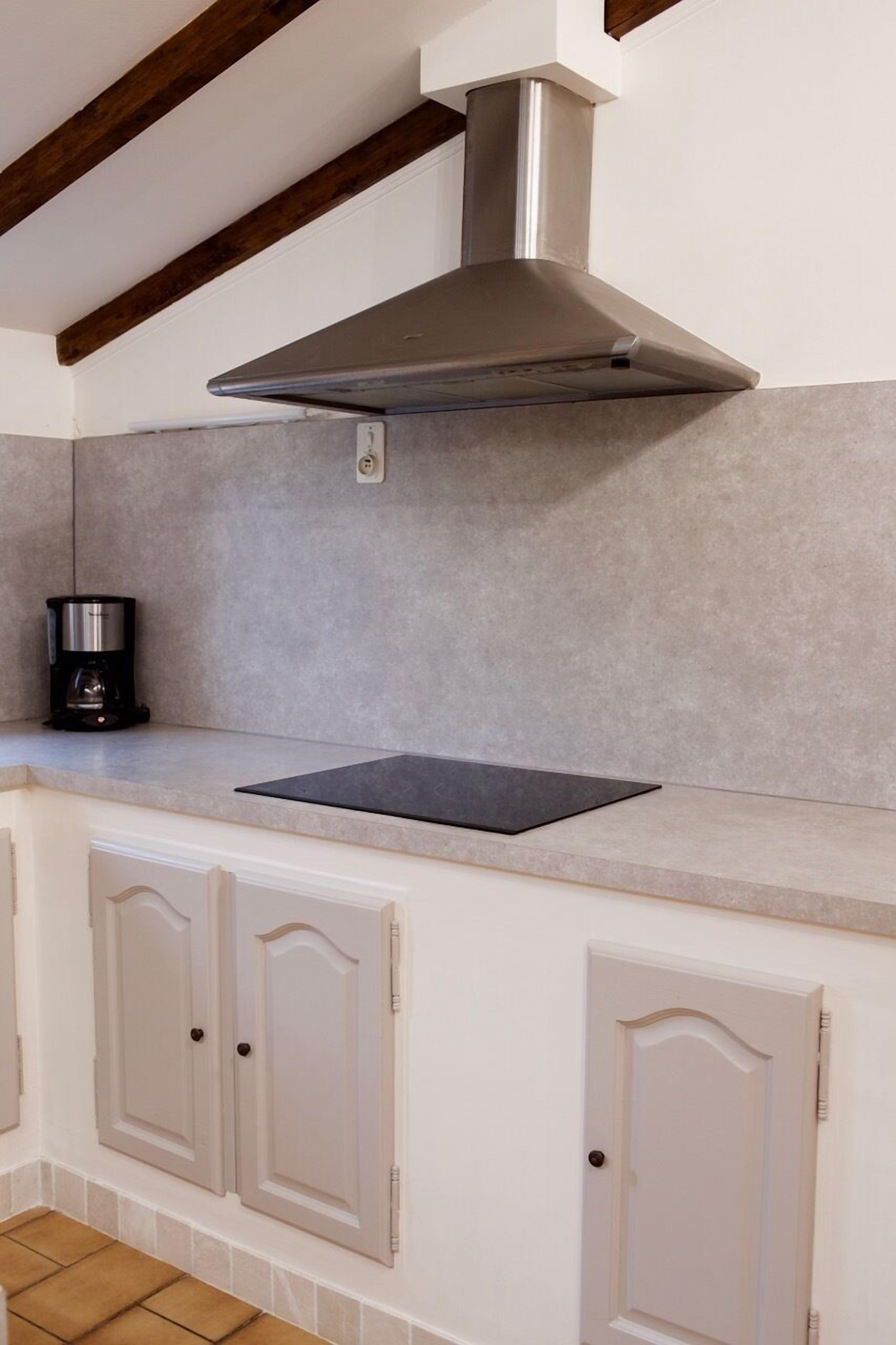 A kitchen with a stainless steel range hood, a black coffee maker, and light-colored cabinets.