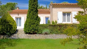 Una casa a due piani con tetto in tegole, pareti bianche e fondamenta in pietra. Sono presenti due porte, una per lato, e una piccola finestra al piano superiore.