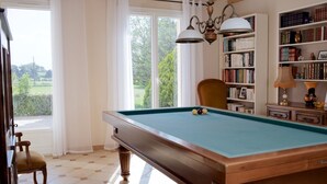 Un biliardo con un telo verde, una sedia di legno e una libreria piena di libri.