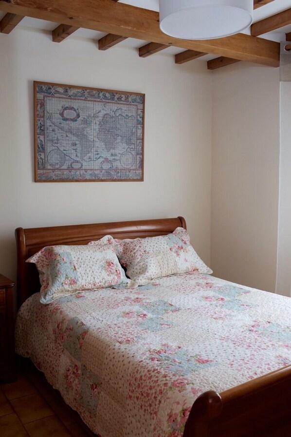 Ein Schlafzimmer mit einem hölzernen Bett, floraler Bettwäsche, einer Karte an der Wand und einem Holzbalken an der Decke.