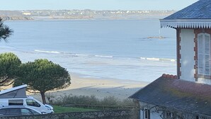 A coastal view with a building featuring a tiled roof and a white facade. - Beautiful family home with sea view and beach access (Lancieux)