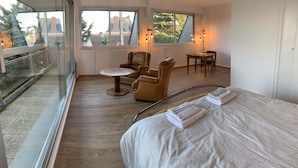 A room with a large window, a round table, two chairs, a small table, and a bed with towels. - Beautiful family home with sea view and beach access (Lancieux)
