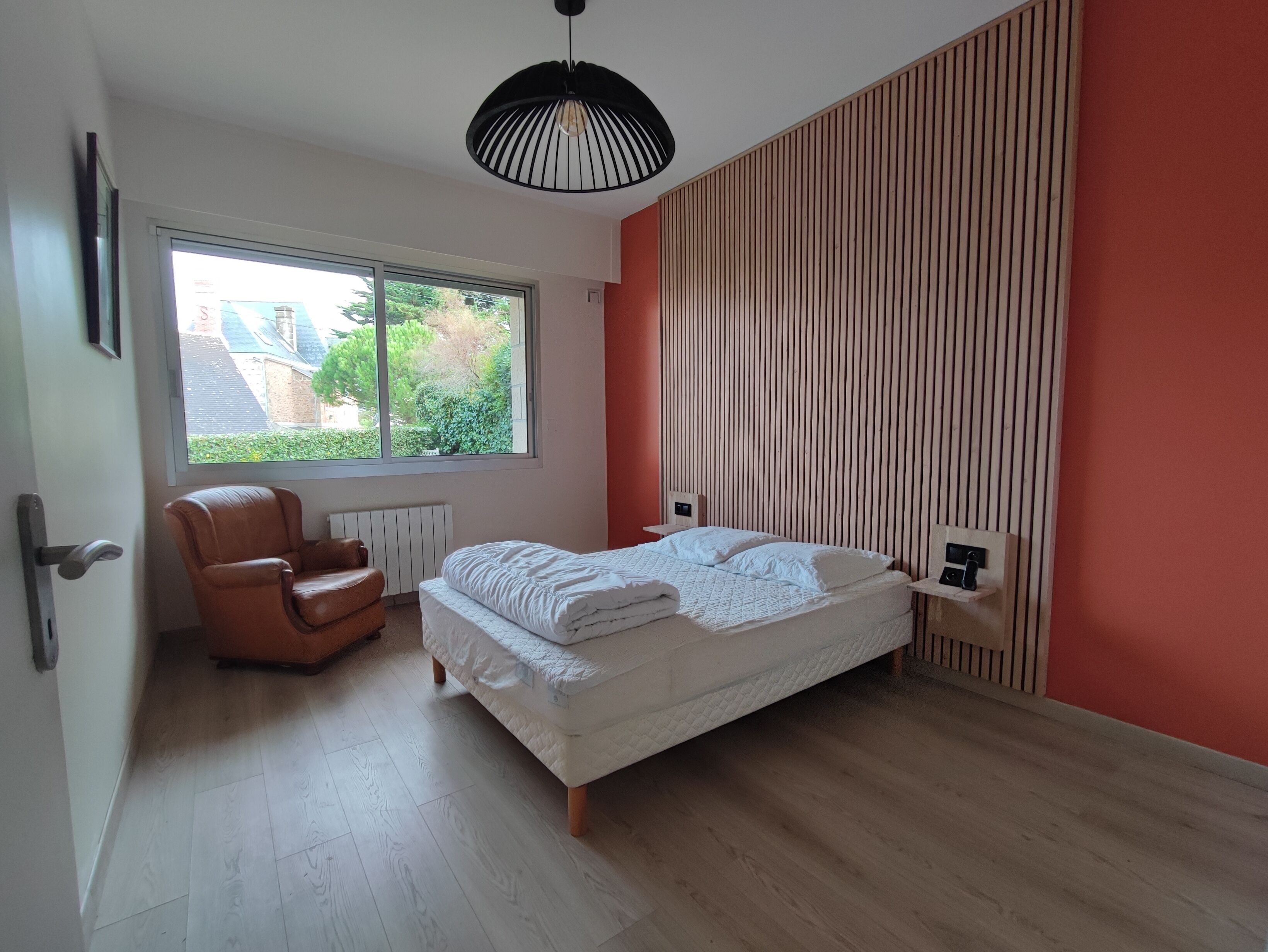 A bedroom with a bed, a chair, a window, and a radiator.