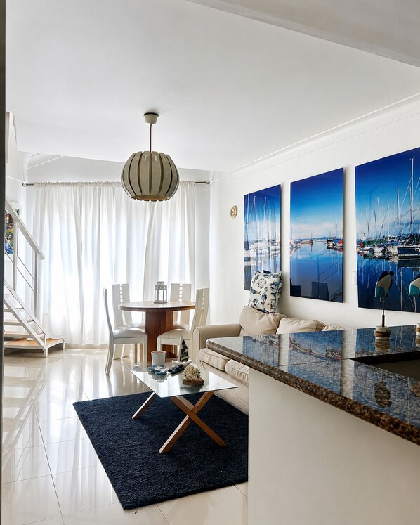 A modern living room with a dining area, a staircase, and a view of the sea through large windows.