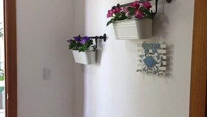 Un couloir avec deux jardinières fixées au mur, ornées de fleurs, un panneau d’accueil et un interrupteur.
