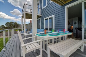 A deck with a table set for dining, outdoor seating, and a view of the house.