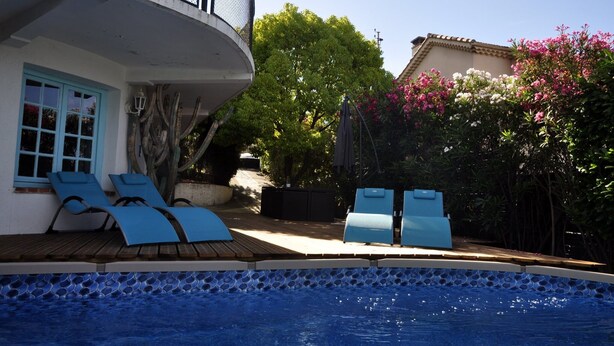 Une piscine avec des chaises longues, une terrasse en bois et une maison dotée d’un balcon.