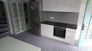 Une cuisine compacte avec des meubles blancs, un plan de travail noir, un four encastré et un réfrigérateur.