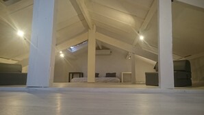 Une chambre spacieuse située sous les combles, avec un plafond en pente, un puits de lumière et un lit agrémenté d’une literie à motifs.