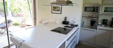 Una cocina moderna con una isla central, hornos empotrados y un ventanal grande.