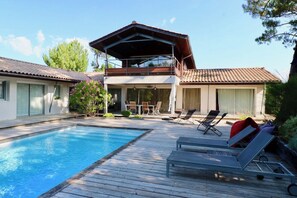 A two-story house with a swimming pool, a covered patio, and lounge chairs. - Exquisite villa with heated pool near beach A3697 (Lège-Cap-Ferret)