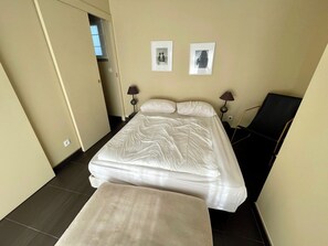 A hotel room with a bed, two bedside lamps, a chair, and two framed pictures on the wall.