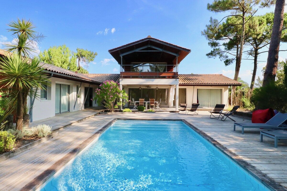 A pool area with a wooden deck, lounge chairs, and a building with a balcony.