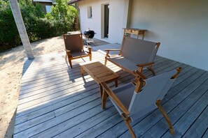 A wooden deck with a table and two chairs, a barbecue grill, and a covered area with a door. - Exquisite villa with heated pool near beach A3697 (Lège-Cap-Ferret)