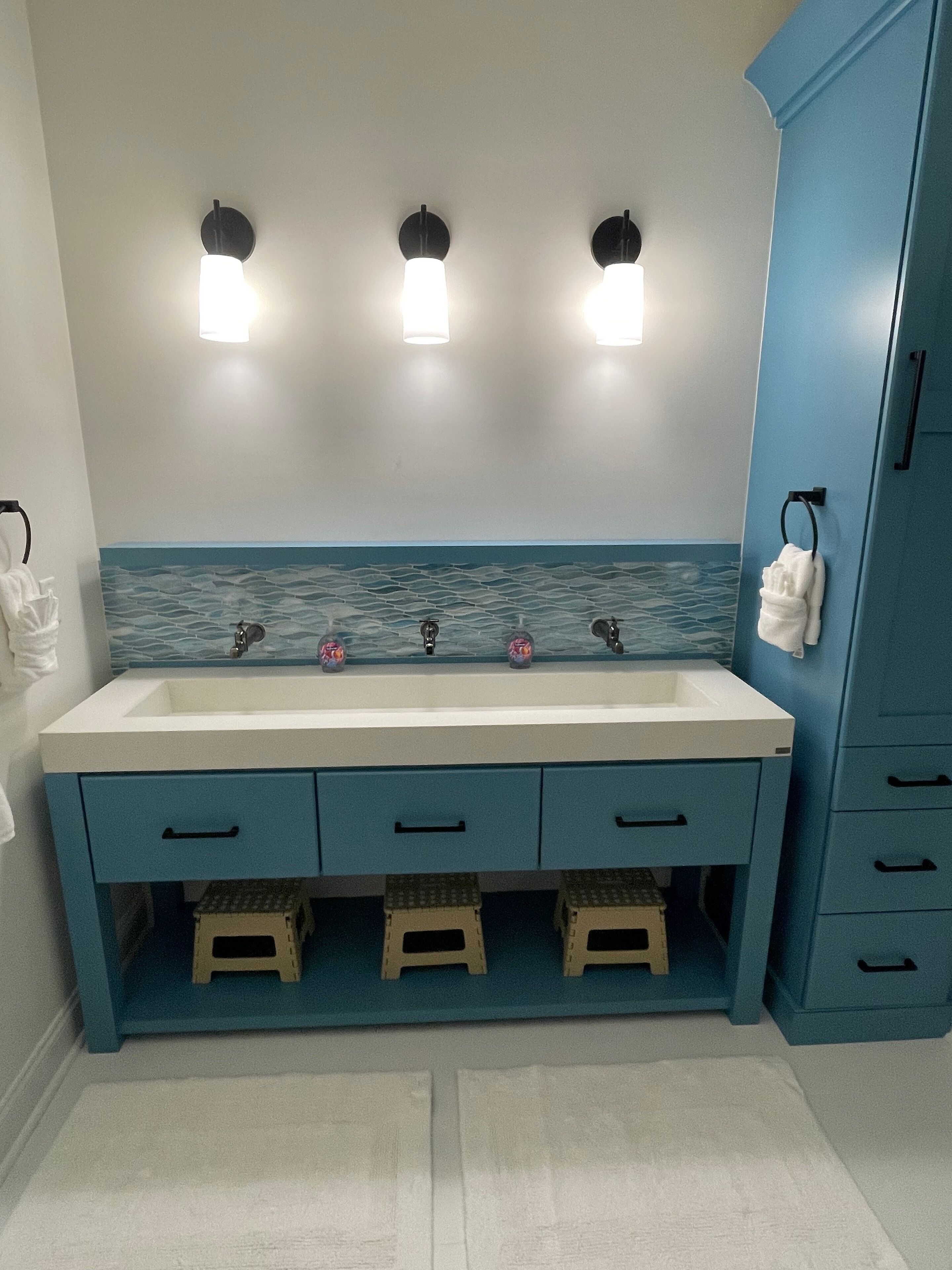 Un baño con un lavamanos grande, tres luces empotradas en la pared y un mueble azul con cajones.