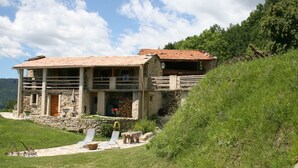 A stone building with a tiled roof, a porch, and a small garden area with a bench and a table. - Former family home : 10 th rental (Braux)