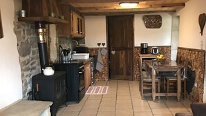 A cozy kitchen with wooden cabinets, a stone wall, and a dining area with a table and chairs. - Former family home : 10 th rental (Braux)