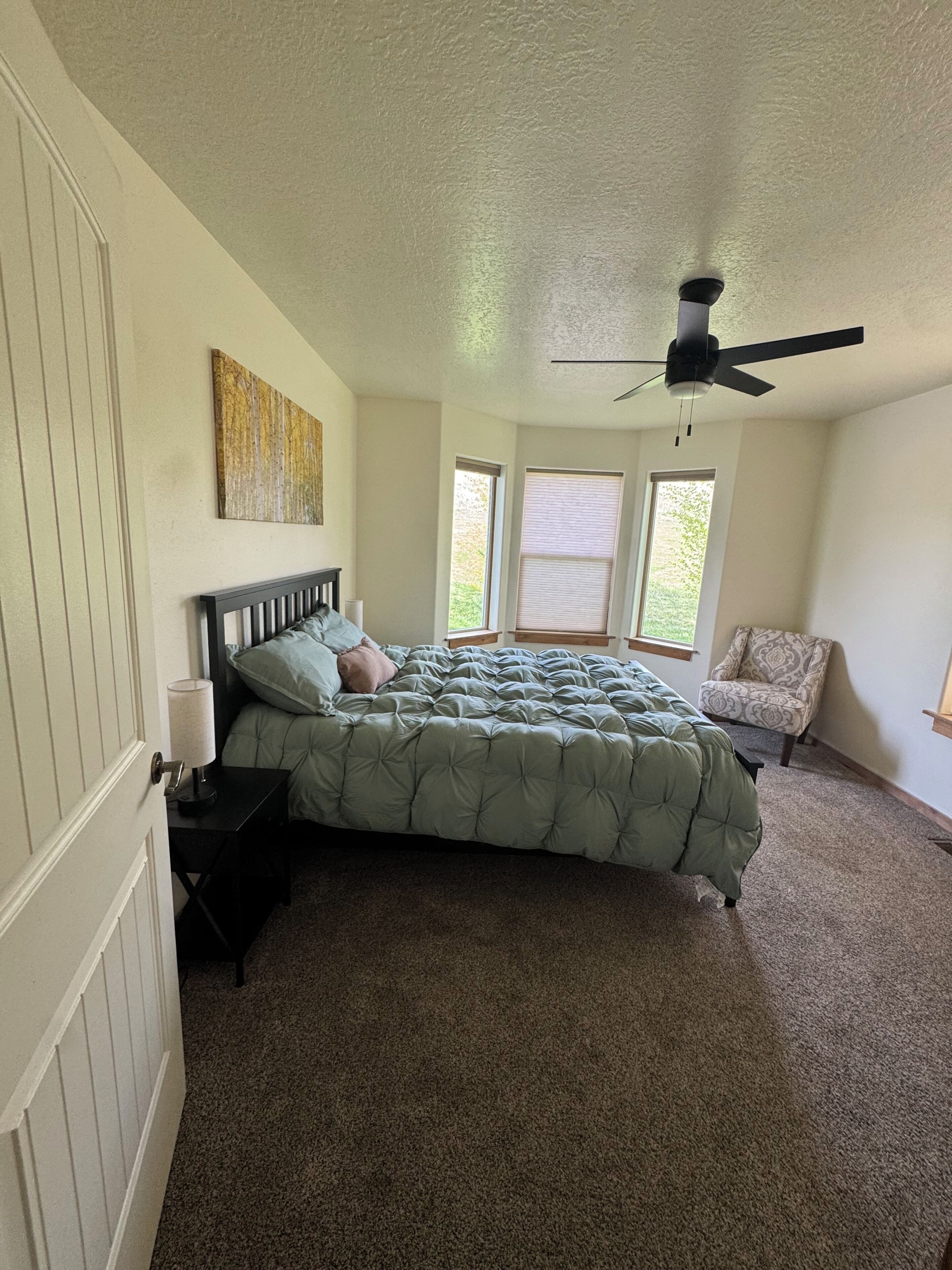 A bedroom with a bed, a ceiling fan, a chair, and a window.