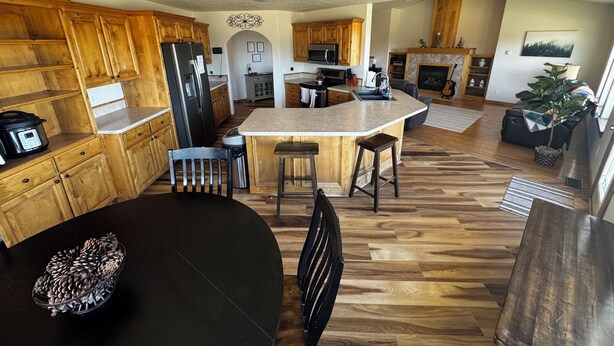 A spacious kitchen with wooden cabinets, a central island, and a dining area with a black table and chairs. - Gateway to Yellowstone, Island Park  (Ashton)