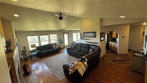 A spacious living area with a large sectional sofa, a ceiling fan, and a kitchen in the background. - Gateway to Yellowstone, Island Park  (Ashton)