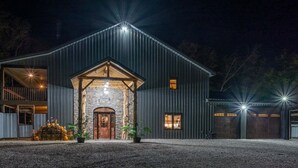 Un ampio edificio in stile rustico a forma di fienile, con un ingresso ben visibile, diverse finestre e un vialetto sterrato.