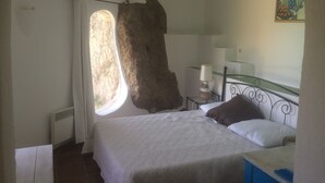 A bedroom with a large window, a bed with white bedding, a bedside table with a lamp, and a painting on the wall. - Large house with private pool quiet with views of the Gulf of Santa Giulia (Porto-Vecchio)