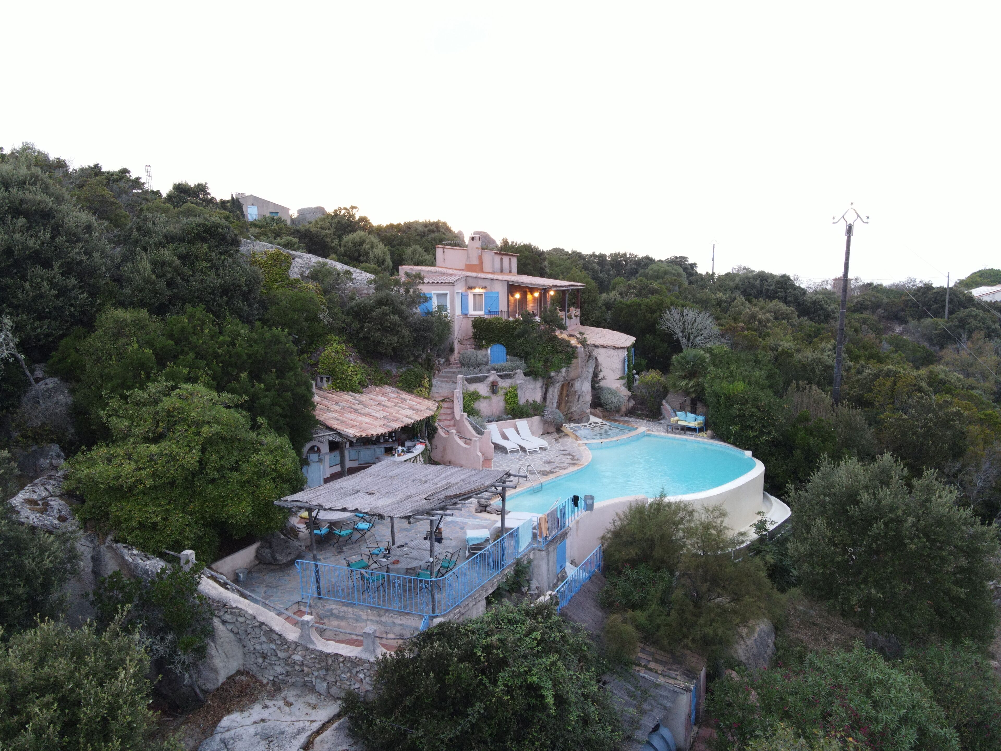 En villa med swimmingpool, omgivet af frodig vegetation og klippelandskab.