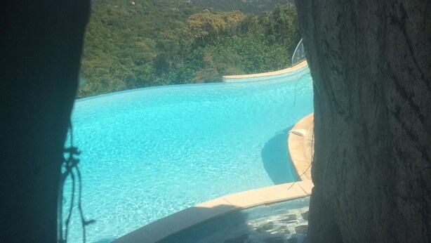A clear view of a swimming pool with a stone floor, surrounded by lush greenery and a rocky cliff. - Large house with private pool quiet with views of the Gulf of Santa Giulia (Porto-Vecchio)