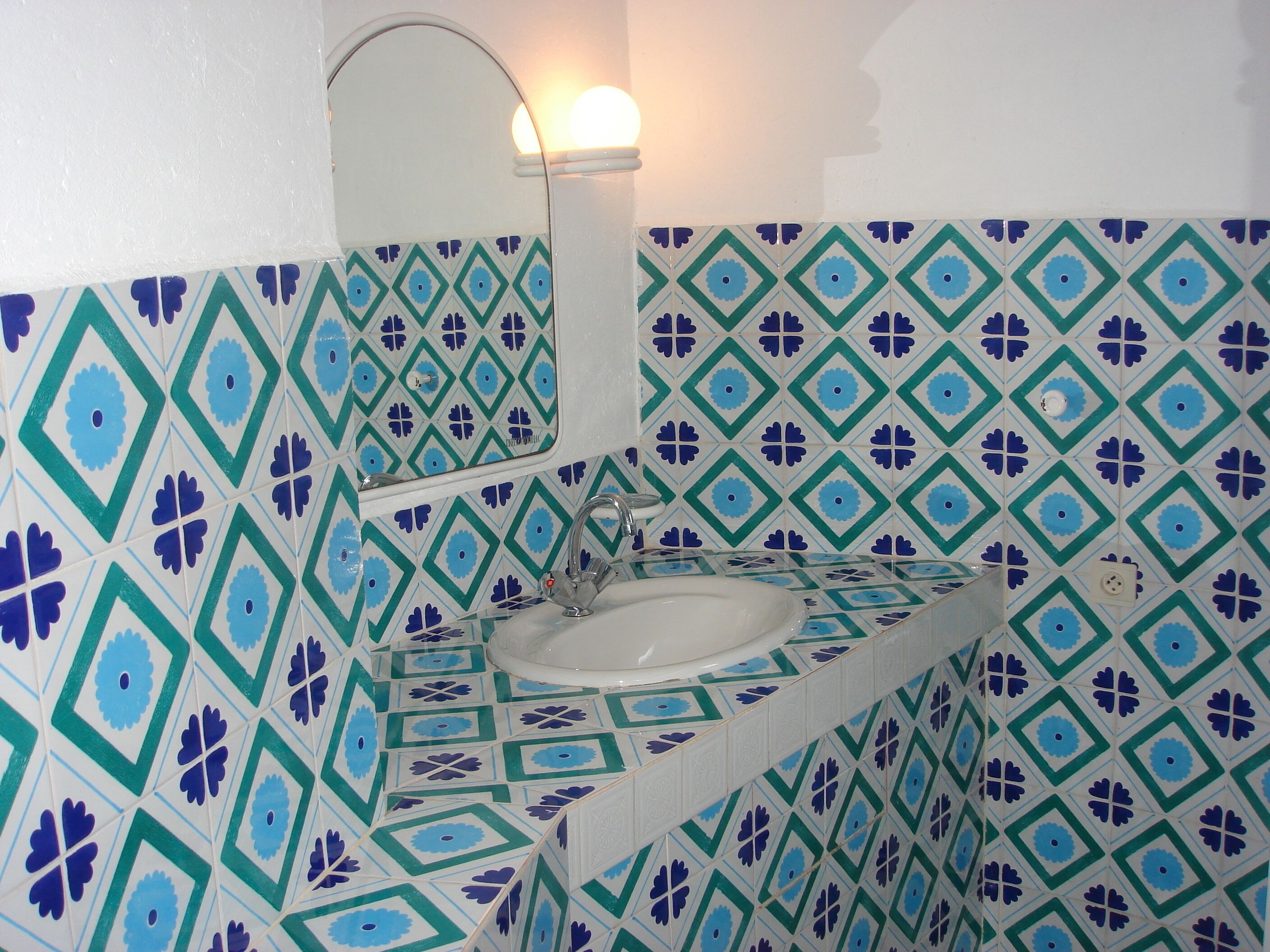 Un baño con lavamanos, espejo y azulejos estampados.