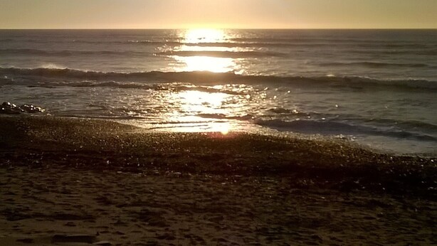 A beach scene with the sun setting over the ocean, creating a calm and serene atmosphere.
