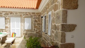 A stone building with a tiled roof, stone walls, and a tiled patio area with a bench and planter.