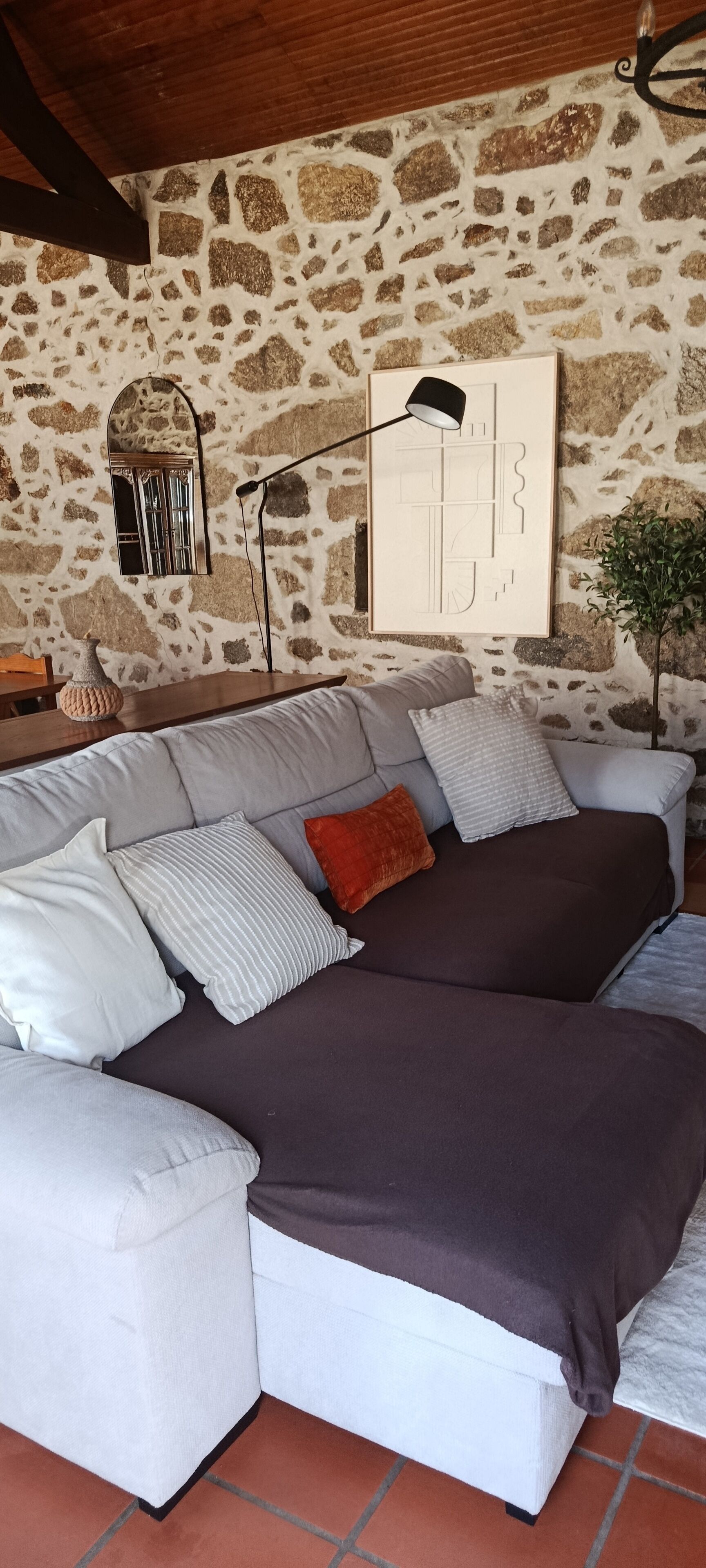 A modern living room with a stone wall, a sofa with multiple cushions, a floor lamp, and a small plant.
