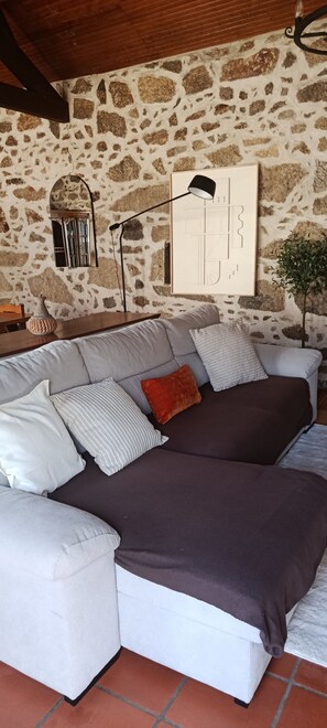 A modern living room with a stone wall, a sofa with multiple cushions, a floor lamp, and a small plant.