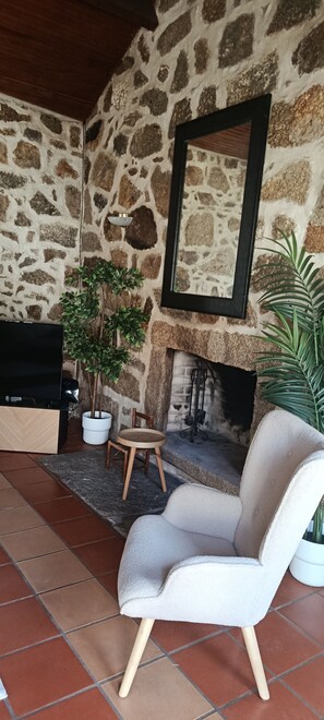 A stone fireplace, a television, and a white armchair in a room with a tiled floor.