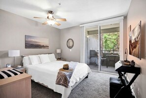 A hotel room with a bed, a ceiling fan, a view through a sliding glass door, a desk, and a chair. - A Perfect Retreat (Chandler)