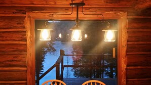 Houten cabinentree met drie hangende lantaarns en uitzicht op een besneeerd landschap.