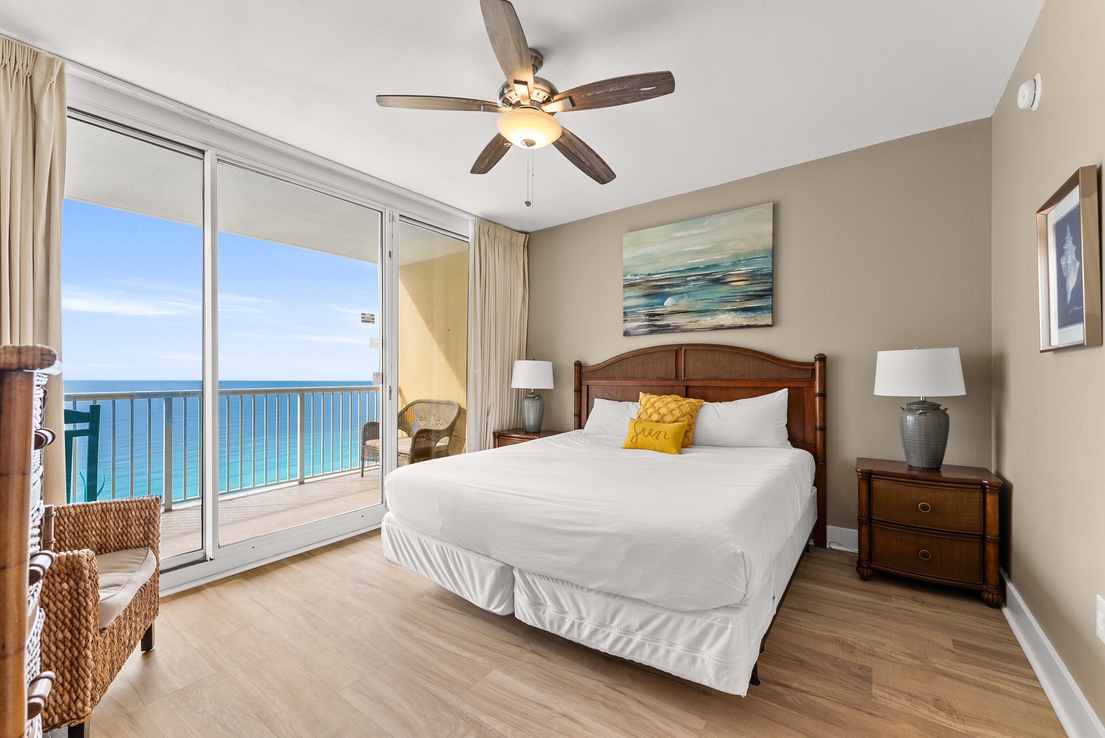 Quarto de hotel com uma cama grande, ventilador de teto, vista para o oceano e varanda com móveis de vime.