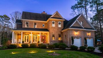A large brick house with a wrap-around porch, multiple windows, and a garage.