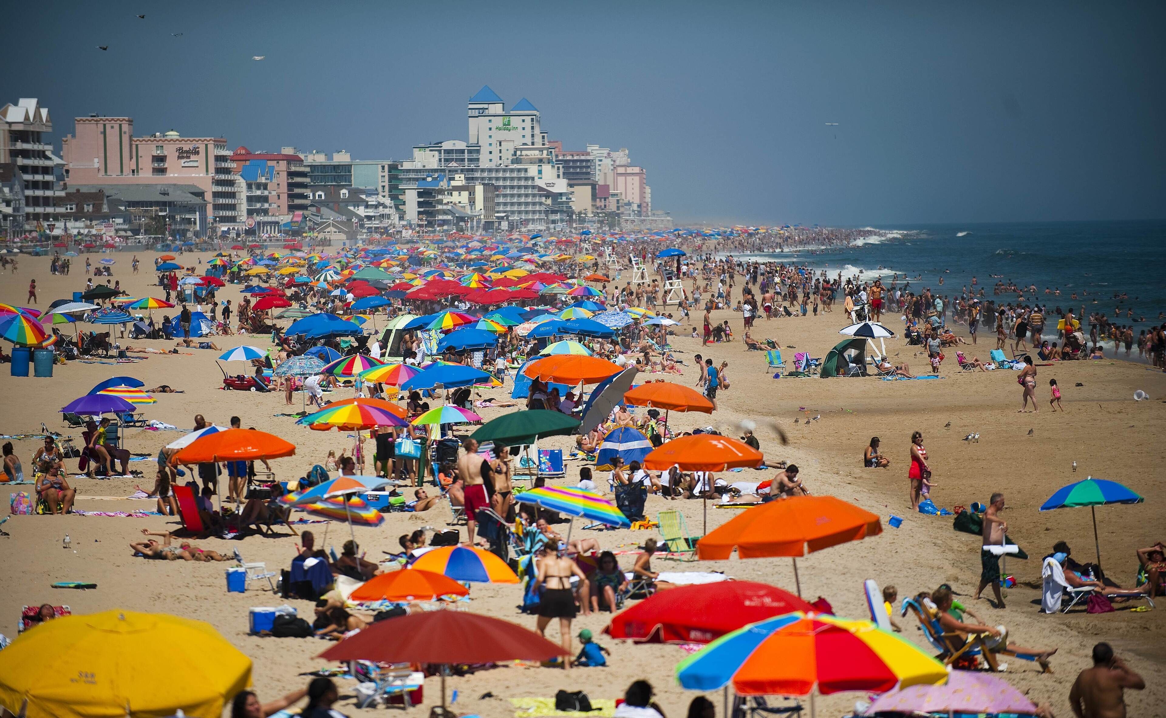 Une plage bondée, avec de nombreux parasols colorés et de nombreux vacanciers.