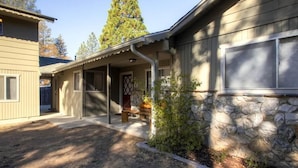 A two-story house with a covered porch, stone foundation, and a large tree in the background. - Lazy Bear Lodge (Oakhurst)