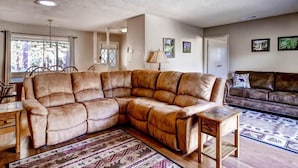 A living room with a large L-shaped sectional sofa, a small wooden side table, and a patterned rug. - Lazy Bear Lodge (Oakhurst)