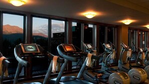 A gym with treadmills and elliptical machines, large windows with a mountain view, and a ceiling with recessed lighting.